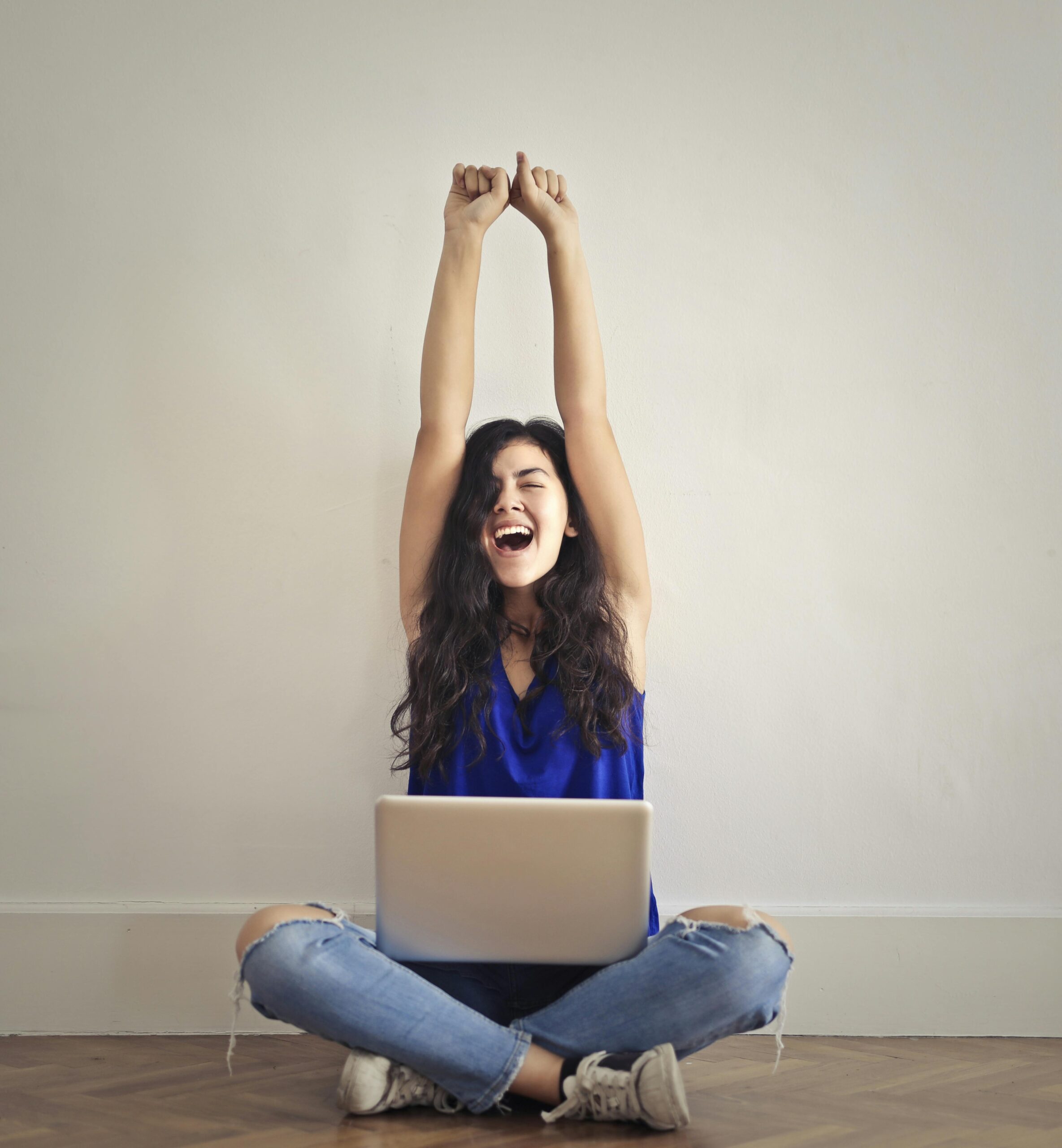 パソコンを膝の上において手を挙げて喜ぶ女性